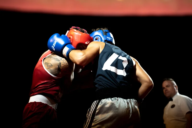 Due pugili in clinch ravvicinato con caschetti blu e rosso durante un combattimento