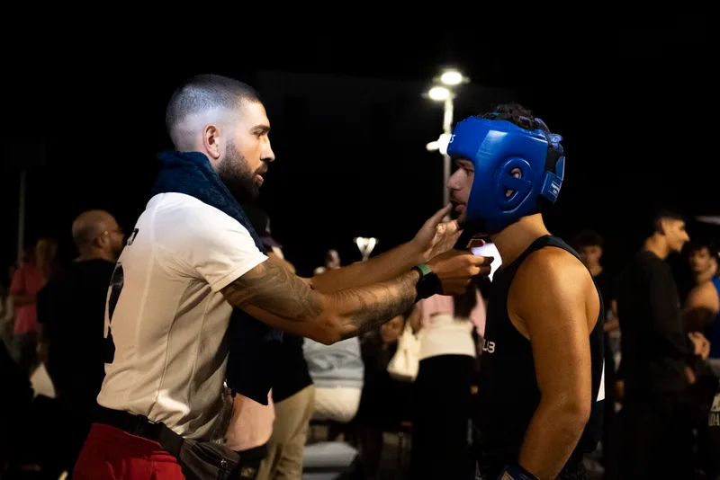 L'istruttore sistema il caschetto al pugile prima del match, momento pre-gara notturno