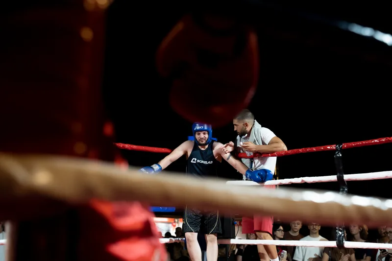 Corner tra un round: l'istruttore consiglia il pugile con caschetto blu all'angolo del ring